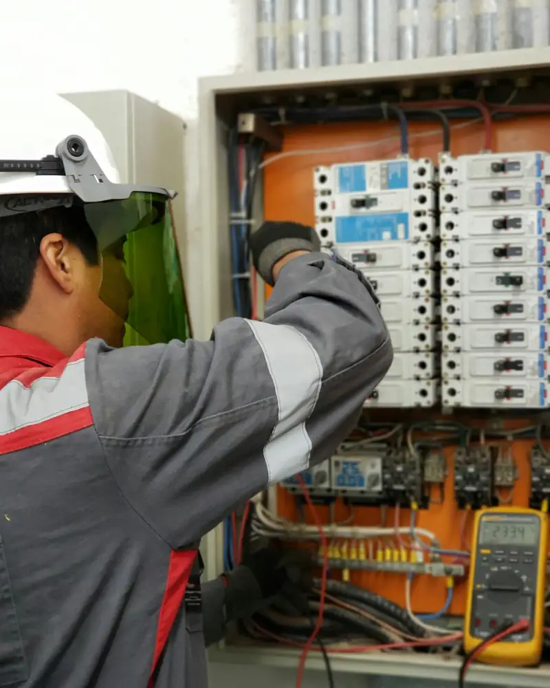 Electrician in protective face shield working inside an electrical control panel